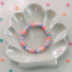 a bracelet is sitting on top of a white flower shaped dish with multicolored beads