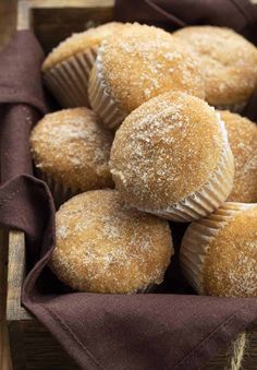 some sugared muffins are in a basket on a table with a napkin