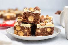 a white plate topped with brownies covered in frosting and toppings next to a cup of coffee