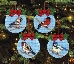 cross stitch christmas ornaments with birds on them hanging from a tree in front of a decorated christmas tree