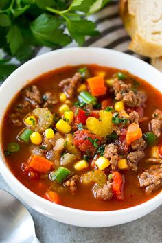 a white bowl filled with meat and vegetable soup on top of a table next to bread