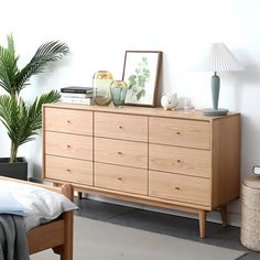 a bedroom scene with focus on the bed, dresser and potted plant in the foreground