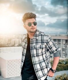 a man wearing sunglasses standing on top of a roof with his hands in his pockets