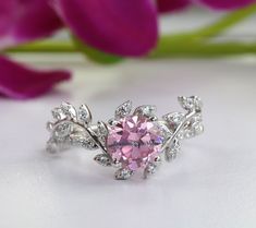 a pink diamond ring sitting on top of a white table next to purple flower petals