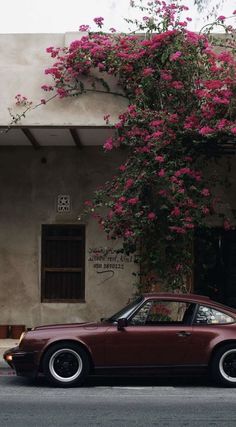 a car parked in front of a building with pink flowers growing on it's side