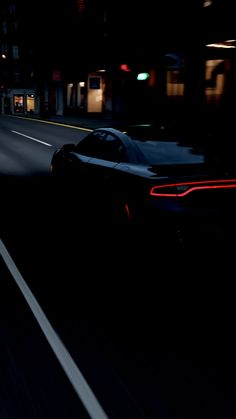 a black sports car driving down a street at night with its headlights on and the tail lights on