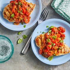 two blue plates topped with chicken covered in tomato sauce and green onions next to a glass of water