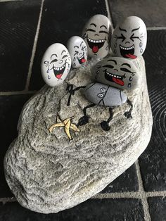 four painted rocks with faces on them sitting on top of a black tile floor next to a stone slab