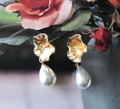 a pair of gold and pearl earrings with flowers in the background on top of a table