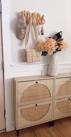 a vase with flowers sitting on top of a wooden cabinet next to a coat rack