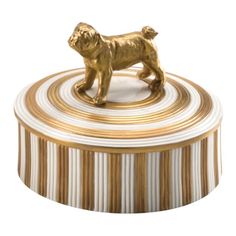 a golden dog figurine sitting on top of a striped box with gold trim