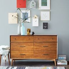 a wooden dresser sitting next to a white wall with pictures on the wall above it