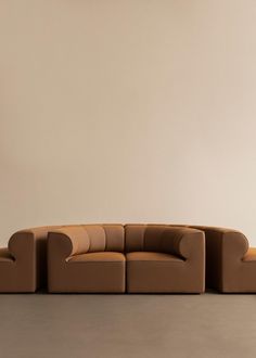 a brown couch sitting on top of a floor next to a white wall and lamp