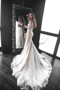 a woman standing in front of a mirror wearing a wedding dress with long sleeves and an open back