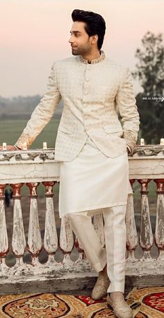 a man standing on top of a balcony next to a railing wearing a white suit