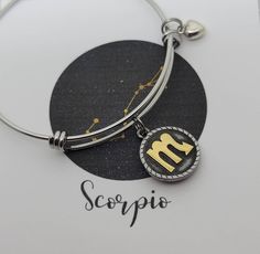 a silver bracelet with a gold zodiac sign on it and the word scorpioo written in cursive writing