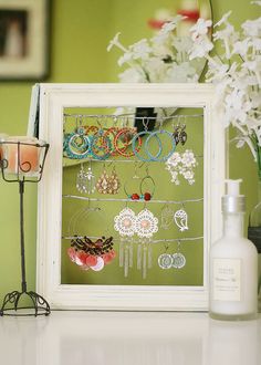 a white frame holding several pairs of earrings next to a vase with flowers in it