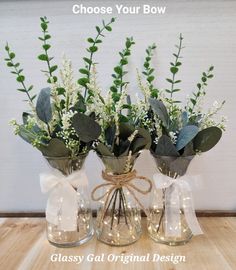 three glass vases with flowers and greenery in them