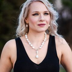 a woman with blonde hair wearing a black tank top and pearls on her necklace is looking at the camera