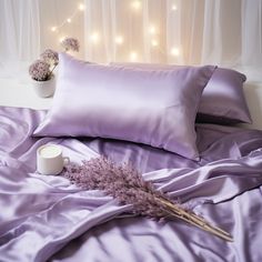 a bed with purple sheets and pillows next to a vase filled with dried lavender flowers