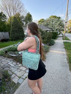 a woman is walking down the sidewalk carrying a purse on her shoulder and looking back