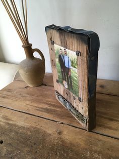 an old photo frame is next to a vase and reeds on a wooden table