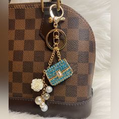 a brown purse with blue and white flowers on the handle is hanging from a gold - tone chain