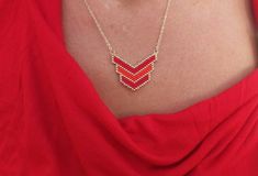 a woman wearing a red top and gold necklace with two chevrons on it