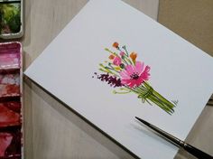 a card with watercolor flowers on it next to some paintbrushes and paints