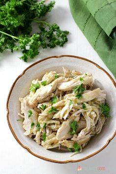 a white bowl filled with chicken and parsley on top of a table next to green napkin