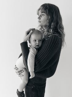 a woman holding a baby in her arms and looking off to the side while wearing a sweater