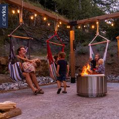 a woman and two children are sitting in hammocks by the fire pit with lights strung over them