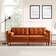 an orange couch sitting in front of a window next to a table with a lamp on it