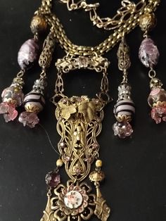 An assemblage of vintage to antique Czech foil glass and Venetian lampwork beads and elements. The central pendant is a Victorian brooch suspending a gilded dress clip from the 1930s. I've added a brooch front at the bottom flanked by two Victorian gold charms and glass from an antique necklace I took apart. Accompanying pendants are vintage filigree brass beads, Venetian lampwork and wedding cake beads with glass flower Venetian posts, vintage rhinestone caps and two large vintage Japanese or Czech foil glass beads. Closes with gold plated links and a brass hook so length can be adjusted. Vintage Gold Necklace With Bead Caps, Vintage Beaded Antique Gold Necklace, Antique Gold Beaded Vintage Necklace, Vintage Bronze Necklace For Party, Vintage Jewelry Bead Caps For Jewelry Making, Vintage Czech Glass Necklaces For Party, Vintage Czech Glass Jewelry For Party, Vintage Glass Jewelry For Parties, Vintage Gold Jewelry With Bead Caps