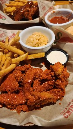 fried chicken, french fries and coleslaw are served on paper wrappers with dipping sauces