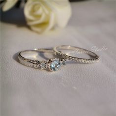 two wedding rings sitting next to each other on a white cloth with a rose in the background