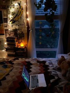 an open laptop computer sitting on top of a bed next to a window covered in fairy lights