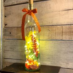 a bottle filled with flowers and lights on top of a wooden table next to a wall