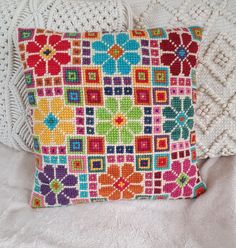 a colorful pillow sitting on top of a bed next to a white crocheted blanket