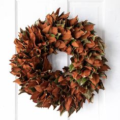 a wreath hanging on the front door of a house that is decorated with orange and green leaves