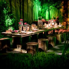 an outdoor dining area with tables and stools, surrounded by greenery at night