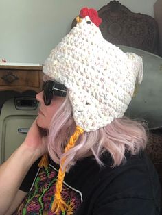 a woman with pink hair wearing a white crochet chicken hat and black sunglasses