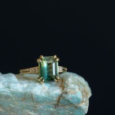 an emerald colored ring sitting on top of a rock