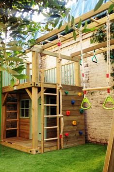 a wooden play structure with swings and climbing bars in the grass next to a brick wall