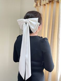 a woman with a white bow on her head looking out the window in front of curtains