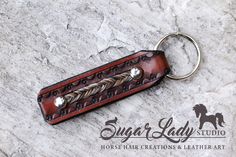 a leather keychain with two metal beads on it's side and a horse logo in the middle