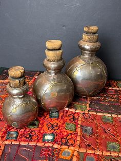 three silver vases sitting on top of a colorful rug next to each other with cork tops