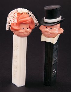 two toy heads are next to each other on a black surface, one is wearing a top hat and the other has a tie