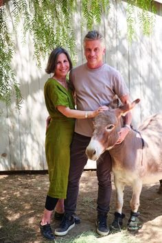 a man and woman are standing next to a small donkey in front of a fence