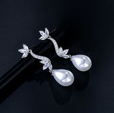 Romantic and elegant, this exquisite pair of earrings features iridescent white pearls and clear cubic zirconia that capture the light from every angle with a perfectly translucent appeal. The earrings are rhodium plated for a bright finish which enhances the intricate detailing and conveys a modern take on old elegance. Overall length of the earring is 38mm (approx. 1.5"). This exquisite design will add a touch of sophistication to any wedding gown or formal ensemble. Luxury Pearl Bridal Earrings With Elegant Design, Luxury Graceful Pearl Earrings For Formal Events, Luxury High Luster Pearl Earrings For Wedding, Luxury Wedding Pearl Earrings With Lever Back, Luxury Timeless Cubic Zirconia Bridal Earrings, Luxury Pearl Earrings With Elegant Design For Formal Events, Luxury Pearl Earrings For Engagement, Luxury Elegant Pearl Earrings For Wedding, Luxury Elegant Pearl Bridal Earrings